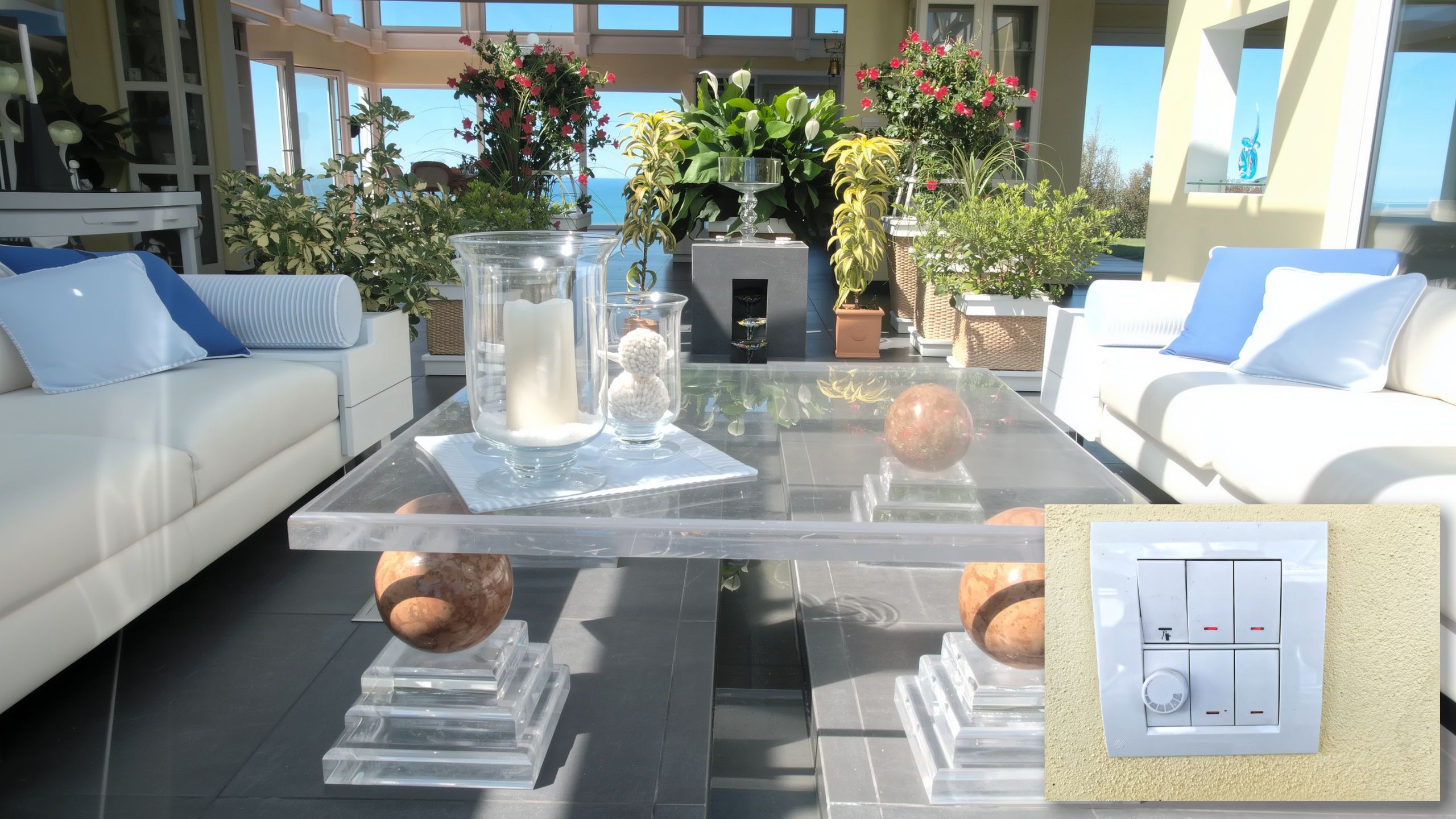 Relaxing family vacation home atrium with houseplants, comfortable seating, ocean views, and light switch detail.