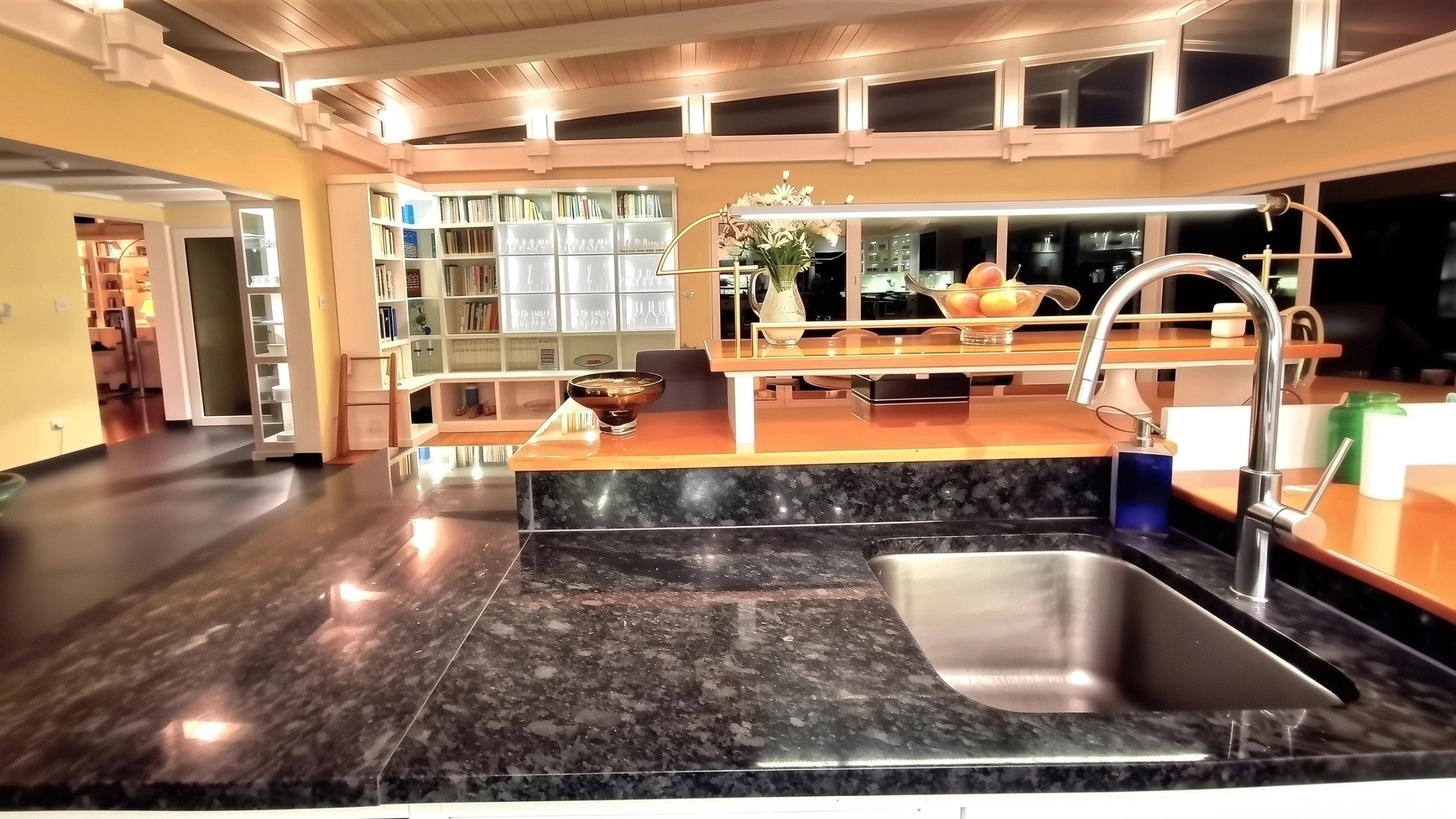 Modern kitchen design sink area overlooking bookcase and dining space in oceanfront property for sale.
