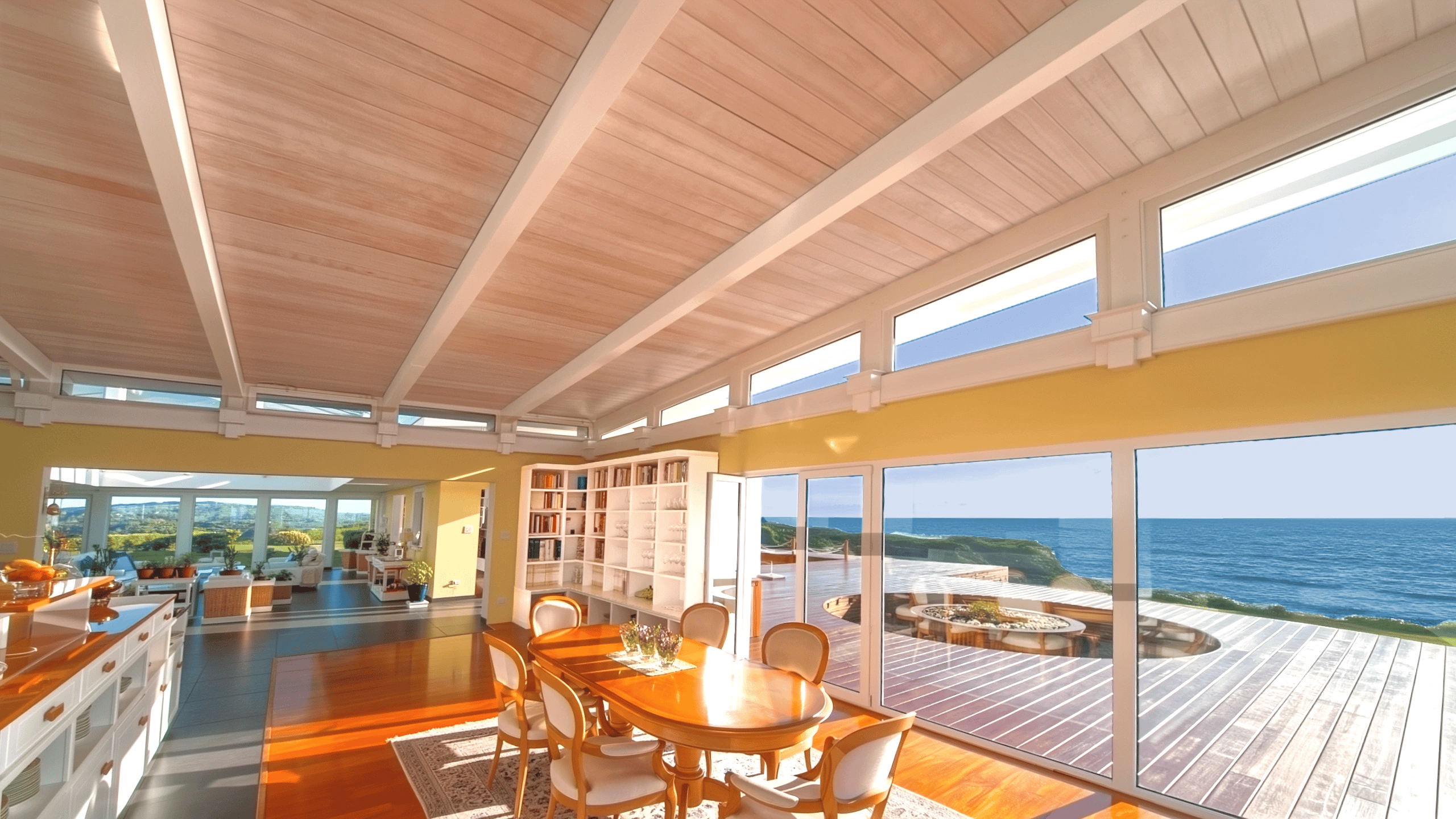 Kitchen open concept view towards dining table set near large windows overlooking ocean deck in house by the sea.