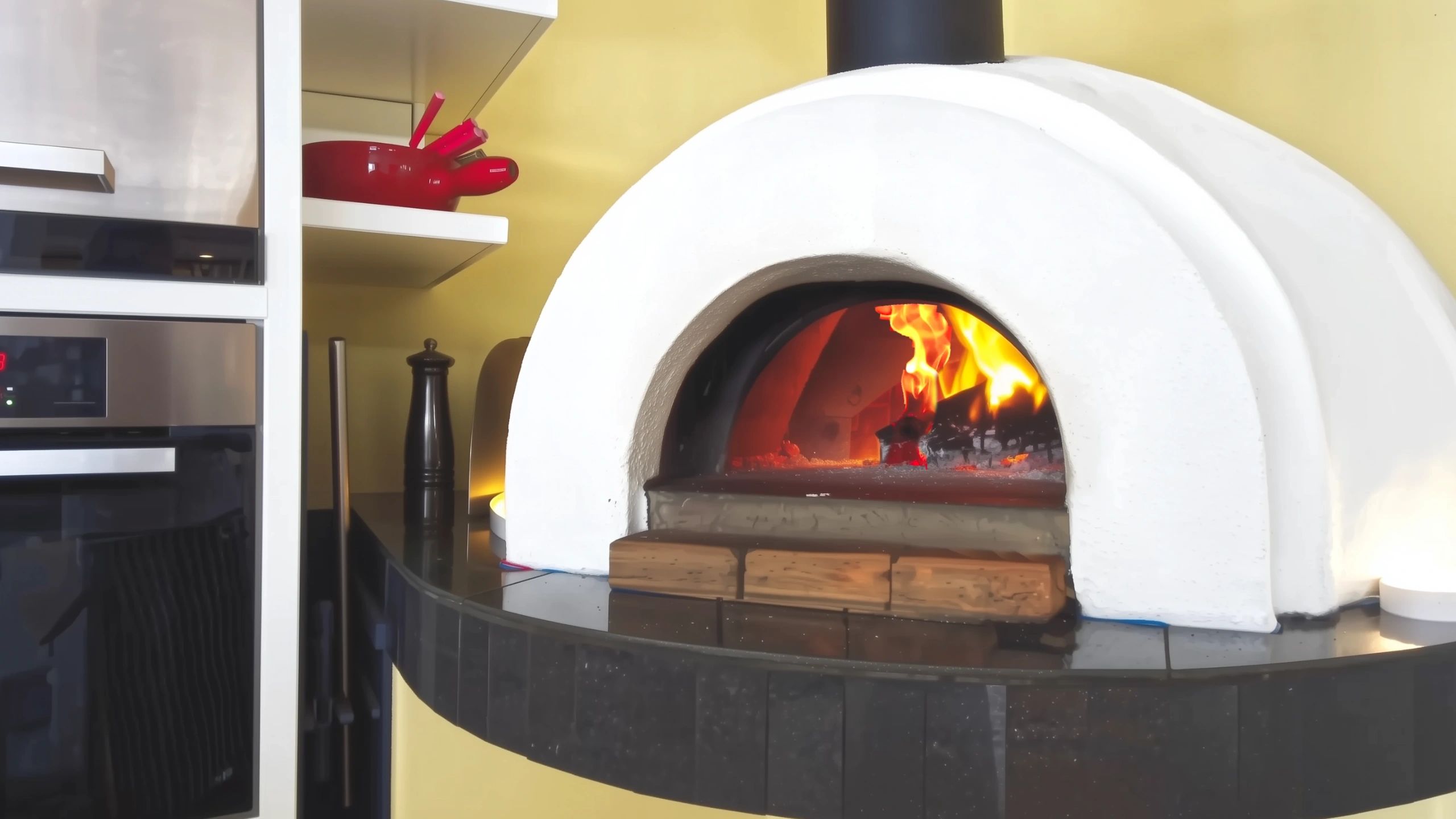 Integrated indoor wood fired pizza oven with burning fire in modern beachside house kitchen.