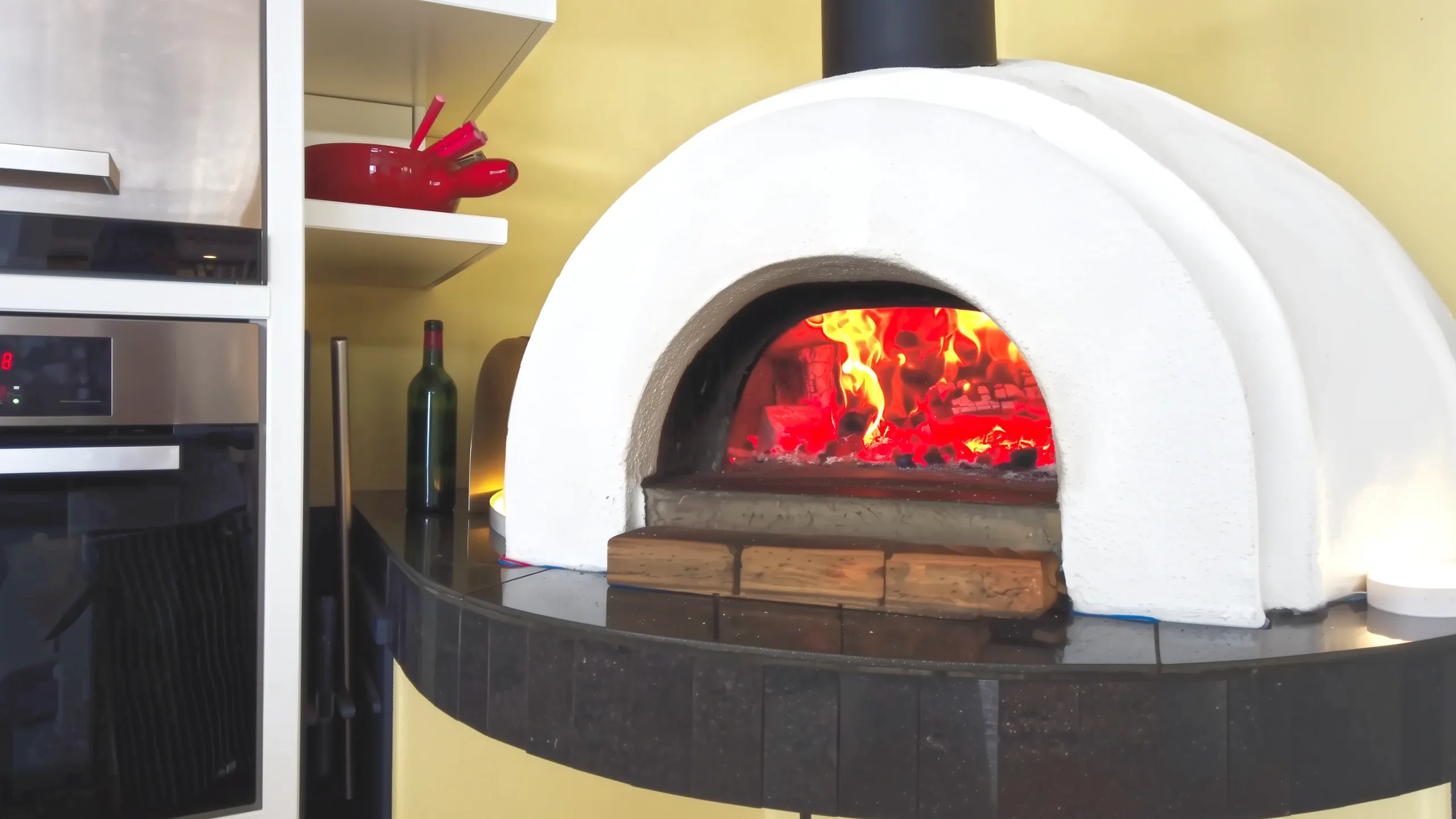 Integrated indoor wood fired pizza oven with burning fire in modern beachside house kitchen.
