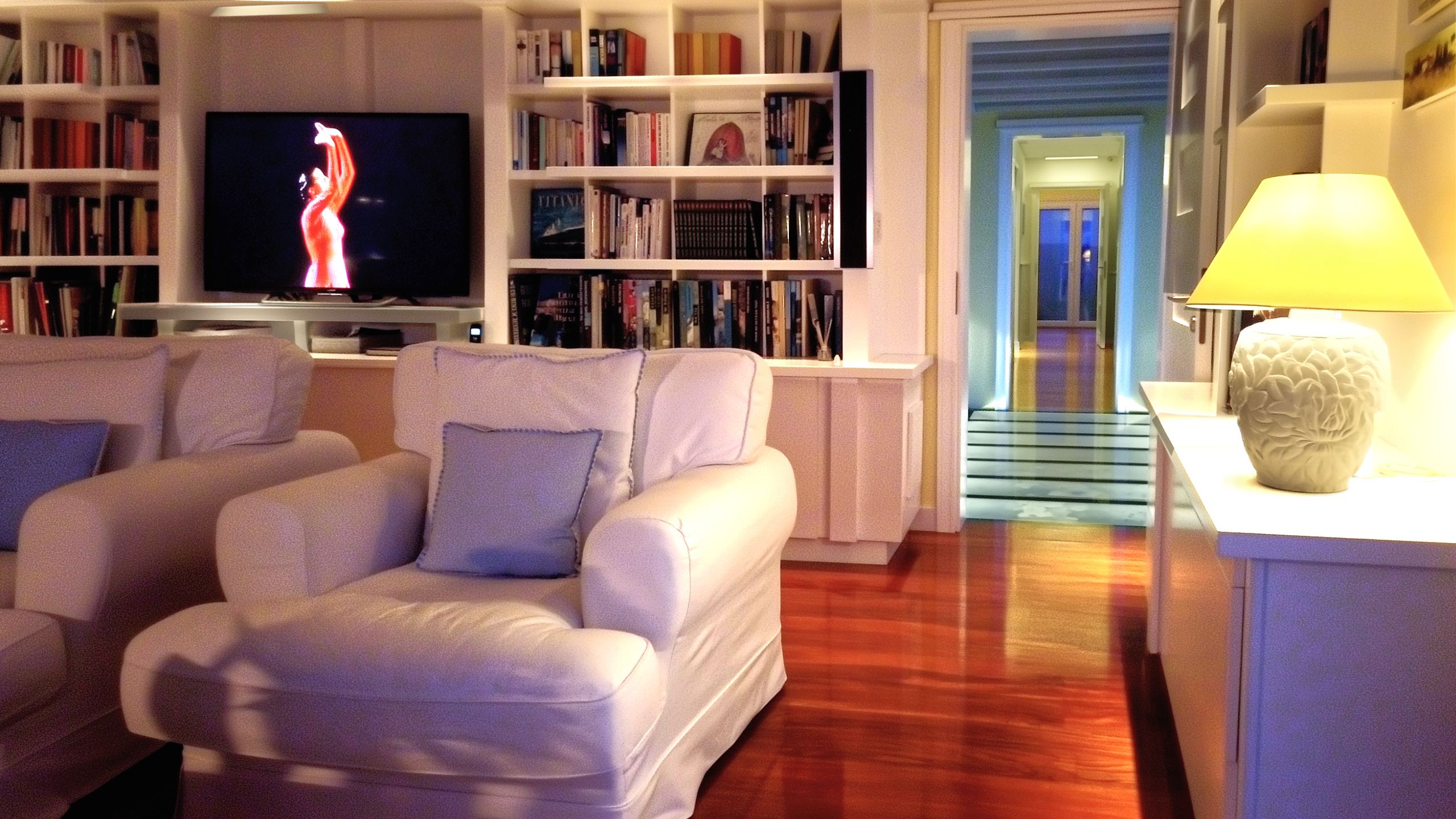 Fully furnished luxury living room at night in turnkey mansion by the beach in NZ, view towards illuminated glass link walkway.